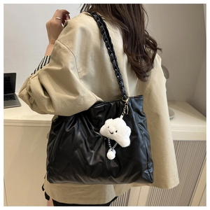 Detail of black quilted leather tote bag with a white cloud plush charm on a wide strap