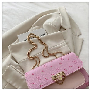 Détail du sac bandoulière rose à fleurs avec chaîne dorée sur un blazer crème