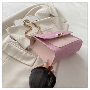 Détail du sac rose en similicuir avec imprimé floral et bandoulière chaîne dorée sur blazer