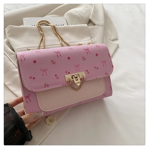 Détail d'un sac bandoulière rose avec motifs nœuds et chaîne dorée sur tissu beige