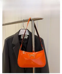 Detail of glossy orange patent leather shoulder bag with gold bow metal buckle hardware
