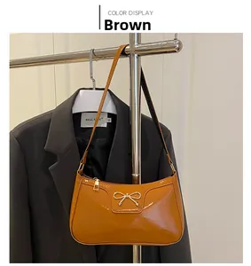 Detail of a brown patent leather baguette bag with a golden metal bow accessory