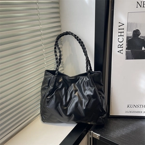 Minimalist black tote bag with wavy pleats and braided shoulder strap on a windowsill