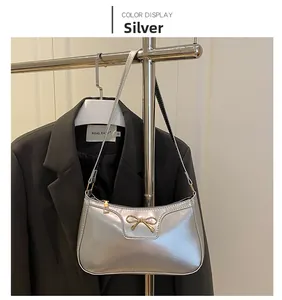 Close-up of metallic silver underarm bag featuring a decorative gold bow and zipper detail