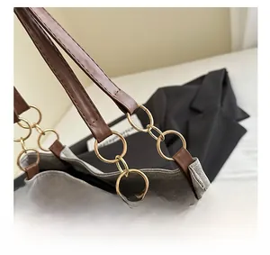 Détail d'un sac en toile gris montrant la bandoulière en cuir et les anneaux dorés