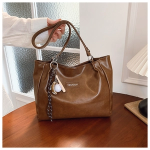 Detail of brown PU leather tote bag with a fashion label and creative baseball keychain