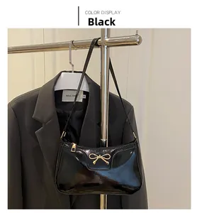 Detailed view of a black patent leather baguette bag with golden bow hardware on a blazer