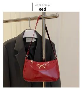 Detail of red patent leather baguette bag with metal bow buckle on display stand