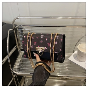 Close-up of black crossbody bag with pink floral patterns and gold metal chain strap