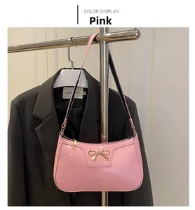 Detail of pink patent leather baguette bag featuring a gold metal bow decoration