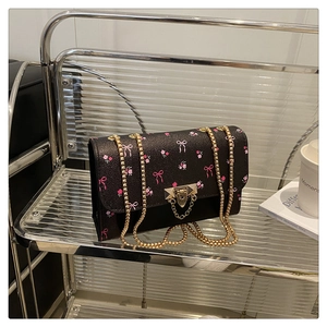 Detail of black crossbody bag with pink floral patterns and golden chain strap