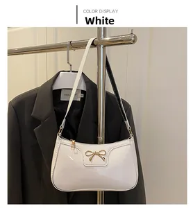 Detail of white patent leather shoulder bag featuring a golden bow metal accessory