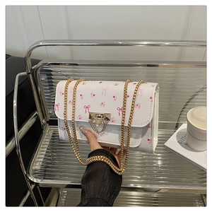 Detail of white chain bag with pink floral patterns and elegant gold metal clasp closure