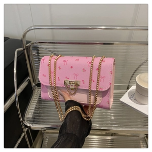 Close-up of pink crossbody bag with red floral bow pattern and gold bead chain strap