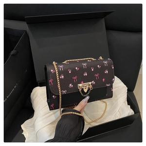 Detail of black crossbody bag with pink bow floral print and gold chain strap in a gift box