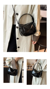 Close-up of black patent leather crossbody bag with silver chain strap and fashion logo