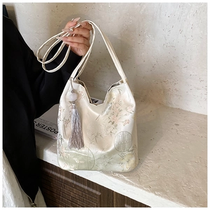 Close-up of beige silk tote bag featuring elegant bamboo embroidery and jade bead tassel