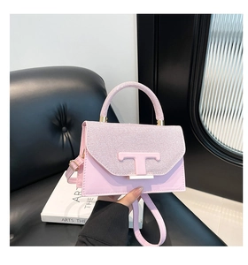 Close-up of pink glitter crossbody bag with metallic T-logo and gold base on dark seat