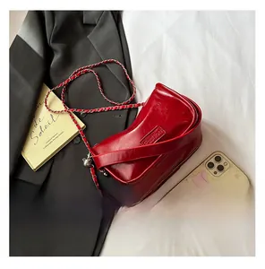Détail d'un mini sac en cuir bordeaux avec chaîne et clochette sur un lit blanc