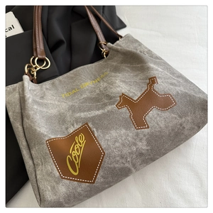 Détail du sac cabas en toile grise avec écusson chien, anses en cuir et texte Tidal