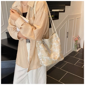 Détail du sac cabas beige avec broderie chinoise dorée et pendentif à pompon gris