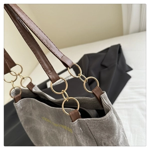 Détail du cabas en toile grise avec bretelles en cuir marron et anneaux en métal doré