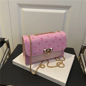 Pink crossbody bag with floral bow print and golden chain strap on a 45-degree angle