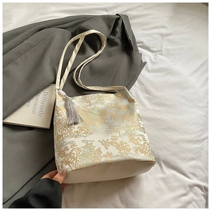 Detailed close-up of cream bucket bag with golden Chinese pattern and silk tassel charm