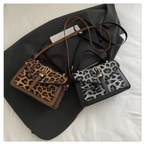 Detail of leopard print crossbody bag with gold buckle and leather trim on grey fabric