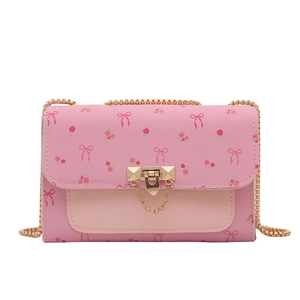 Pink cherry blossom crossbody bag with bow patterns and gold chain strap in studio light
