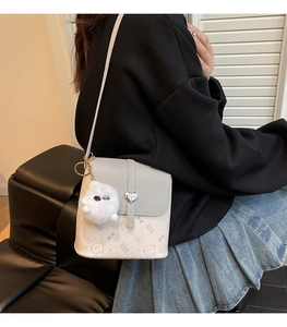Close-up of contrast color crossbody bag with heart lock and soft white fur ball pendant
