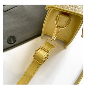 Detail of yellow leather bag showing golden metal buckle and rhinestone trim on edge