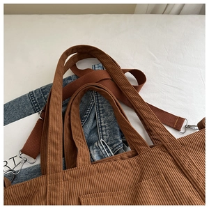 Brown corduroy tote bag with dual handles and detachable woven strap on denim background