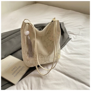 Detail view of floral embroidery and grey tassel charm on chic bucket bag