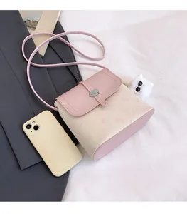 Pink and beige crossbody bag with heart clasp and cat pattern next to a smartphone