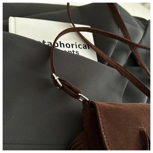 Détail d'un sac bandoulière en daim marron avec pompon et boucle argentée réglable