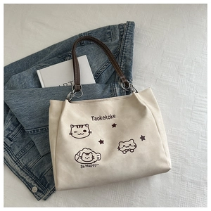 Detail of canvas tote bag with cute cat prints, leather handles, and metal ring accents