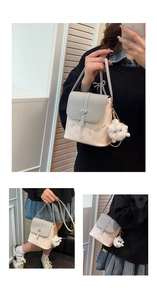 Detail showing creamy white and gray crossbody bag with heart buckle and fur ball