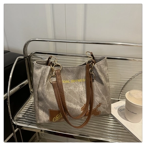 Détail du cabas en toile grise avec anses en cuir marron et logo sur un support