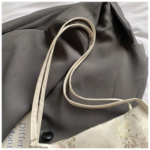 Detailed close-up of floral embroidery texture and leather strap on a cream bucket bag