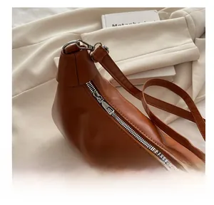 Close-up of smooth metal zipper and textured brown PU leather on crescent shoulder bag