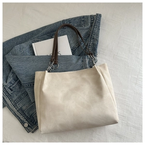 Detail of minimalist tote bag showing cream matte fabric and brown leather handles