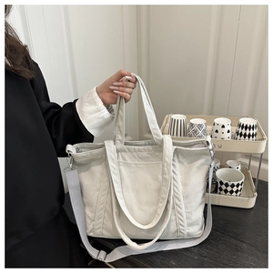 Detail of off-white corduroy tote bag featuring adjustable strap and front pocket