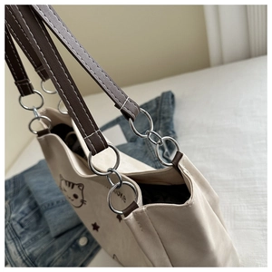 Detail of canvas tote bag showing silver metal ring connectors and brown leather handles