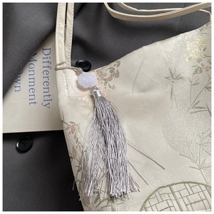 Detail of beige jacquard fabric with floral patterns and a long silver tassel charm