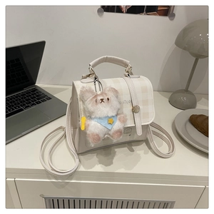 Detail of cream plaid backpack with plush bear pendant on a minimalist desk setting