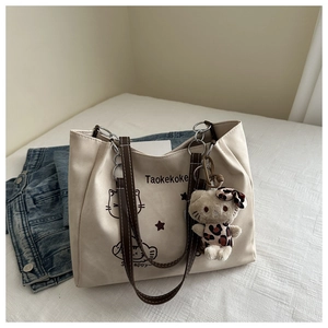 Detail of beige canvas tote with cat print and leopard plush charm on a shoulder strap