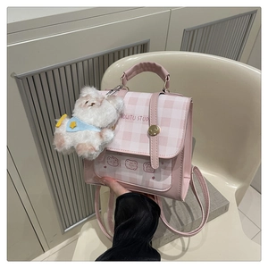 Detail view of pink plaid leather backpack featuring a cute cartoon bear pocket and plush charm