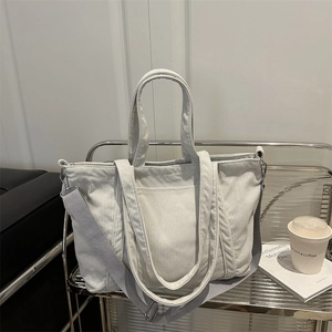 Cream corduroy tote bag with dual handles and grey adjustable shoulder strap in modern setting