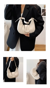 Detail of a minimalist white crescent shoulder bag featuring adjustable strap and gold buckle